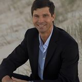 A man in a suit sitting on the beach.
